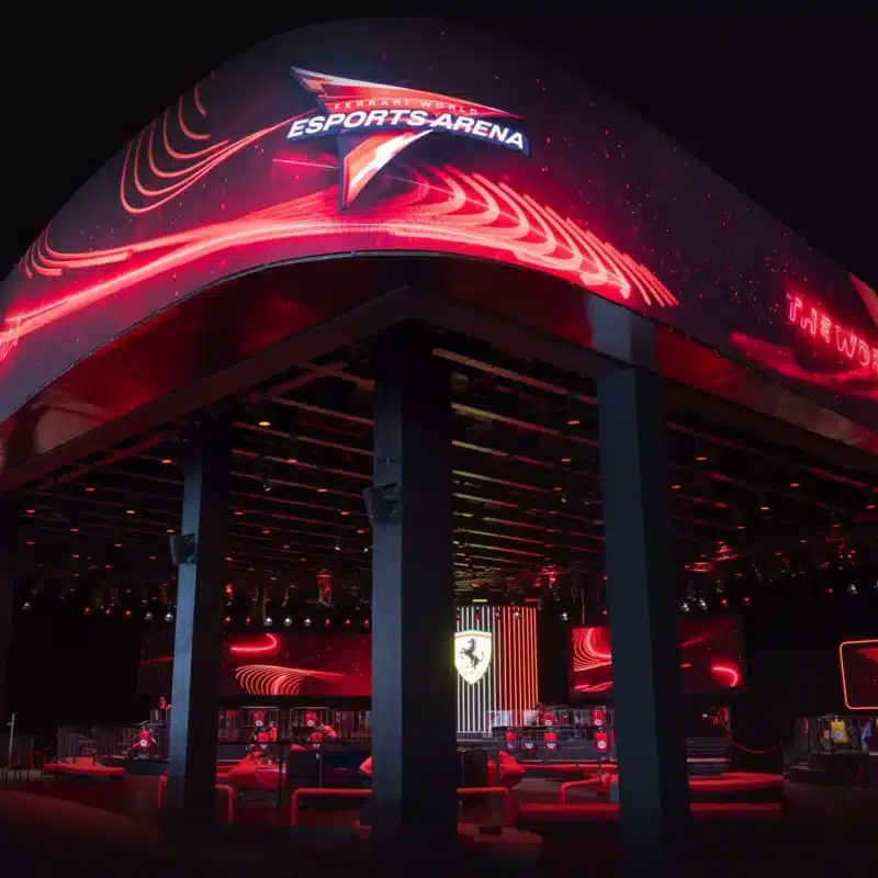 Immagine che raffigura il Ferrari World Esports Arena vista dall'esterno con nome e logo Ferrari in evidenza. Image that represents the Ferrari World Esports Arena seen from the outside with the Ferrari name and logo highlighted.